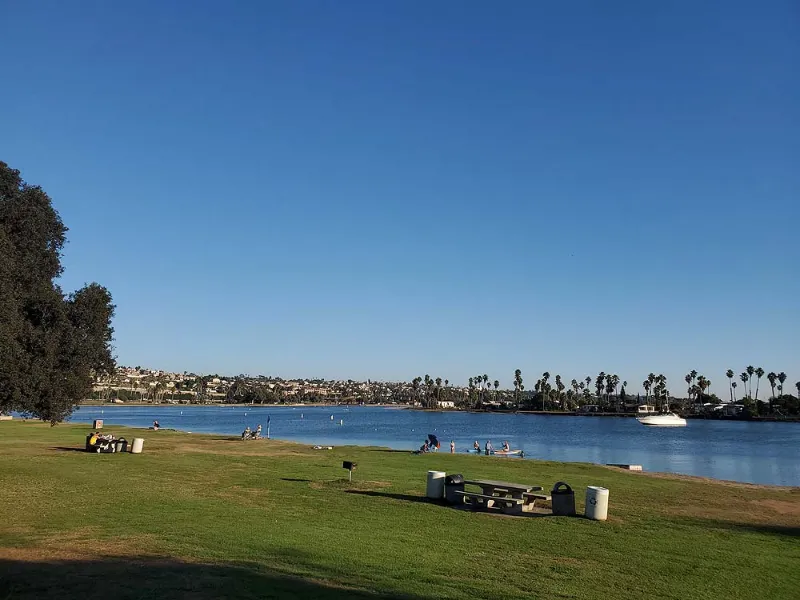 De Anza Cove on Mission Bay, flat sheltered water with grass and picnic tables along the shore and paddleboarders out on the bay.
