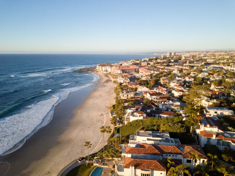 The La Jolla coastline at low sun, a long beach with small waves breaking along it and houses on the bluff above.