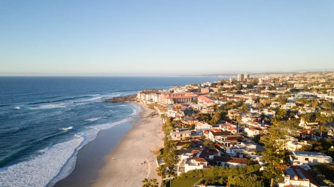 The La Jolla coastline at low sun, a long beach with small waves breaking along it and houses on the bluff above.
